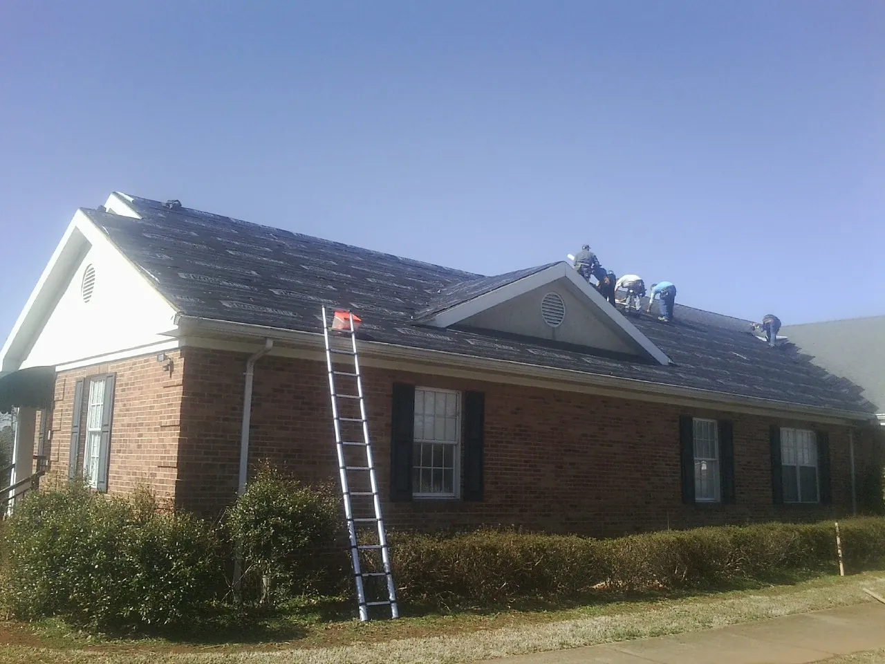 Crew tearing shingles off a brick ranch roof with a ladder set — Emergency Roof Repair work by our crew in Kents Store