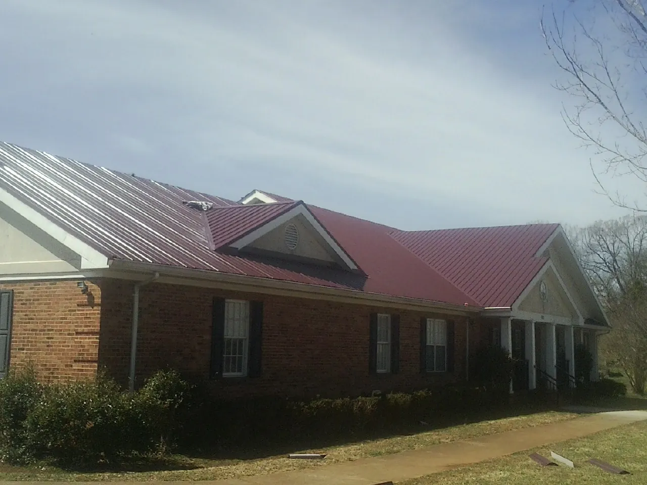 Red metal roof with gabled entries on a long brick building, from a Hail Damage Roof Repair job in Kents Store