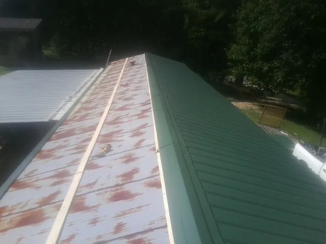Old rusted panels beside newly installed green metal roofing — Wind Damage Roof Repair by Roofing Brothers in Kents Store