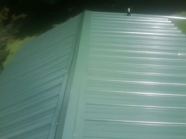 New green metal panels meeting at the ridge of a roof — Flat Roof Repair work by our crew in Kents Store