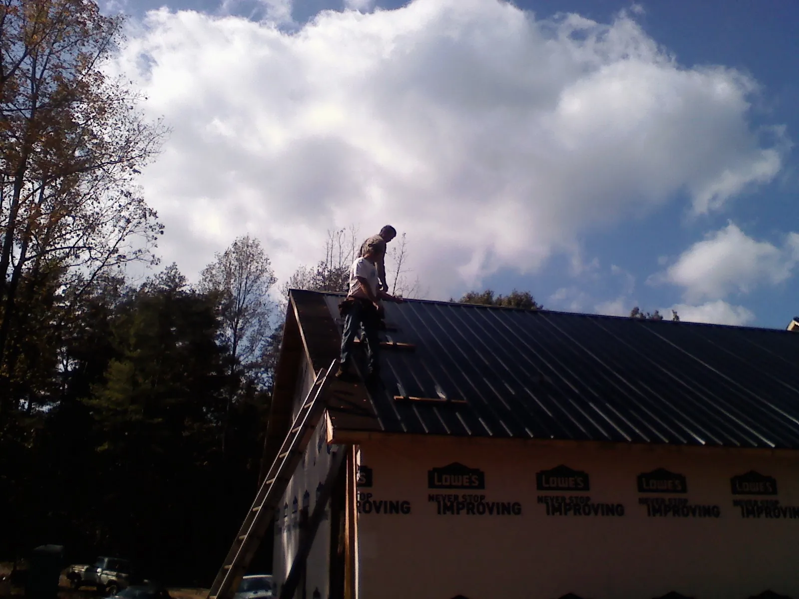 Roofer fastening dark metal panels high against a cloudy sky, from a Roof Inspection job in Kents Store