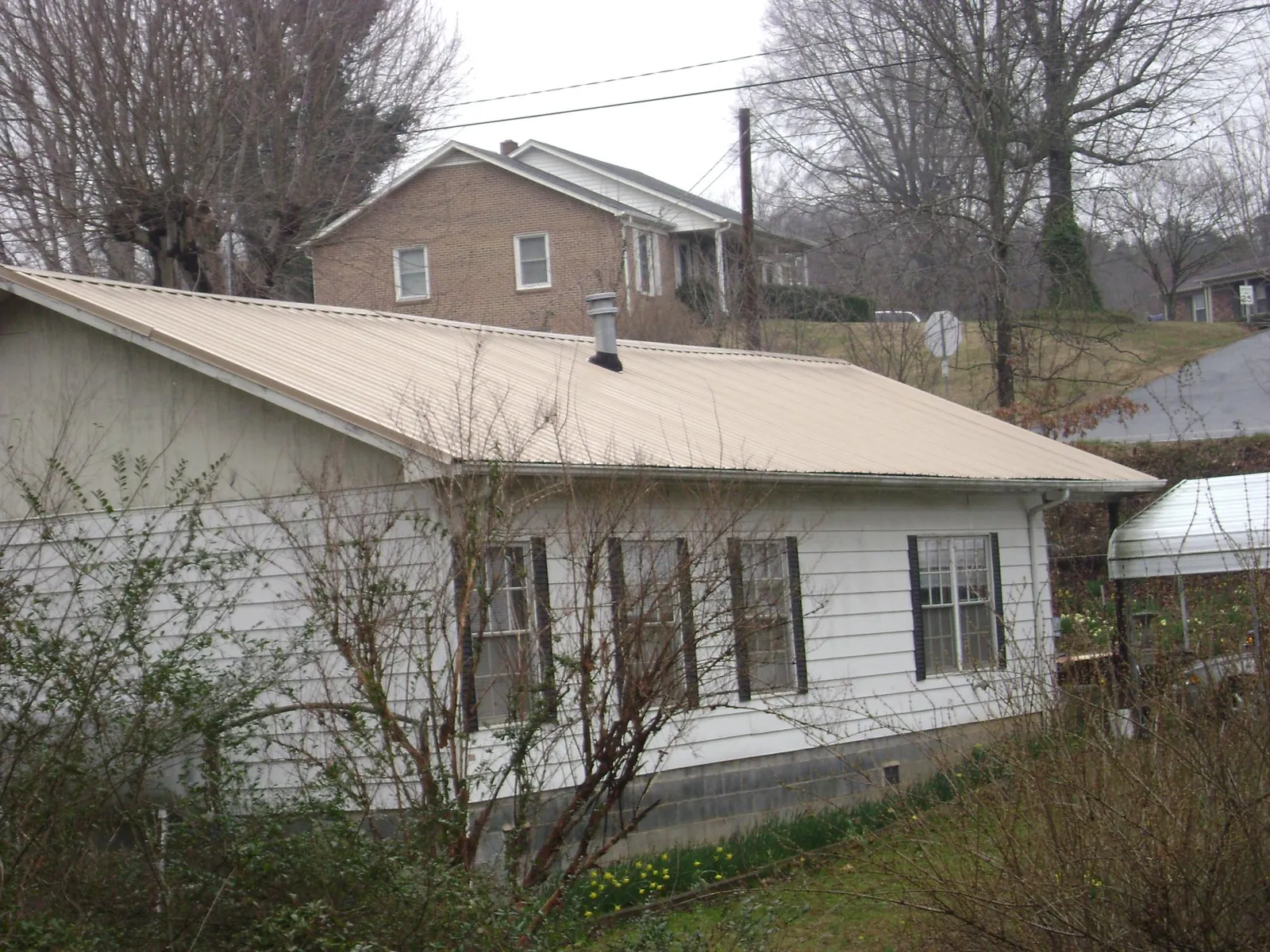 Tan metal roof on a white sided house set into a hillside — Commercial Roofing by Roofing Brothers in Kents Store